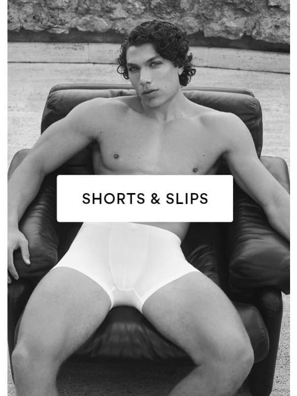 Schwarz/Weiß-Bild eines Männermodels, das in einem schwarzen Leder-Sessel sitzt und eine weiße Shorty der Serie 10 out of 10 trägt.