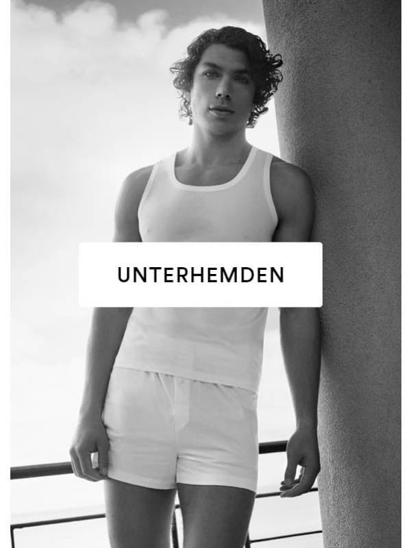 Schwarz/Weiß-Bild eines Männermodels, das an einer Säule angelehnt in weißer Boxershorts und weißem Athletic-Shirt der Serie mey 10 out of 10 gekleidet ist.