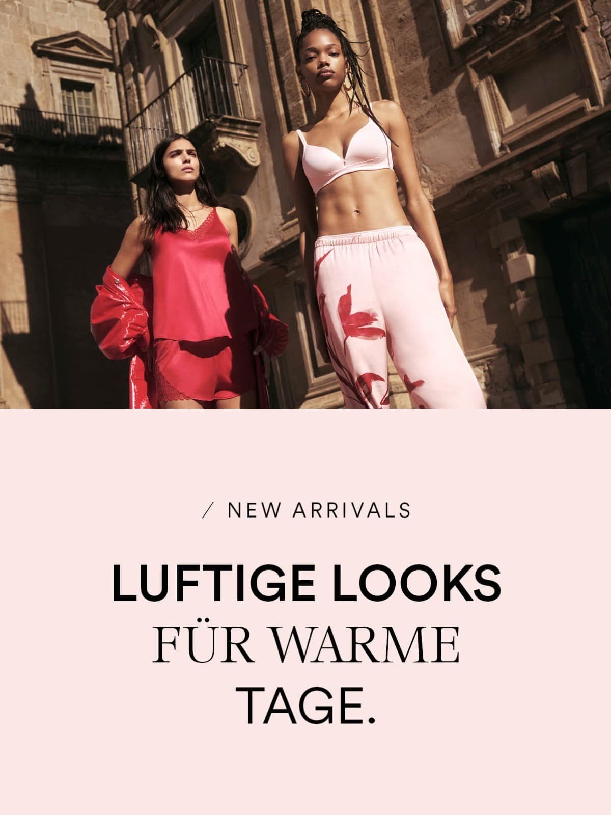 Zwei Damenmodels posieren vor einem Gebäude. Das Model auf der linken Seite trägt ein Set aus Camisol und French Knicker in der Farbe Red Carpet. Das Model auf der rechten Seite trägt ein BH und eine lange Schlafhose in der Farbe Bonbon Pink.
